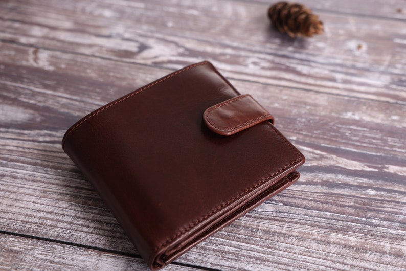 May include: A brown leather wallet with a flap closure. The wallet is folded and lying on a wooden surface.