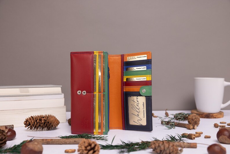 May include: A multi-colored leather wallet featuring a red exterior, an orange interior, and various card slots in yellow, green, and blue. The wallet includes a clear ID window, a snap button closure, and a card insert labeled Genuine Leather.