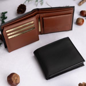 May include: A black bifold wallet shown in both closed and open positions. The interior is tan leather with multiple card slots, each containing a gold-colored card labeled Genuine Leather, and a coin pocket with a flap closure.