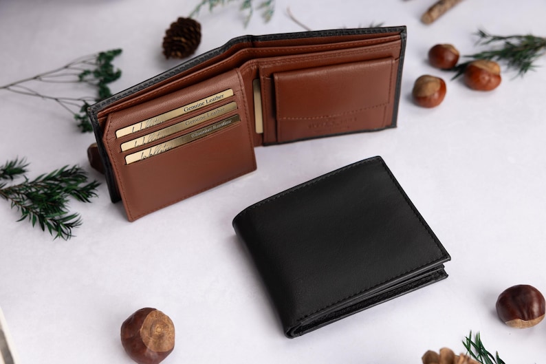 May include: A black bifold wallet shown in both closed and open positions. The interior is tan leather with multiple card slots, each containing a gold-colored card labeled Genuine Leather, and a coin pocket with a flap closure.