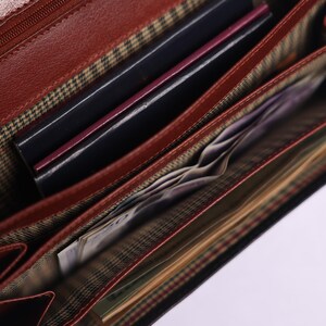 May include: Open brown leather wallet with multiple compartments. The wallet is filled with cash and cards.