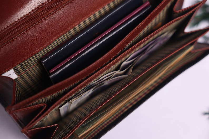 May include: Open brown leather wallet with multiple compartments. The wallet is filled with cash and cards.