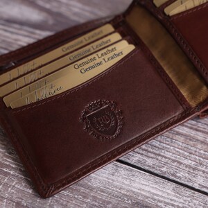 May include: A brown leather wallet with multiple card slots and a gold embossed logo. The wallet is open and the inside is lined with a beige fabric.