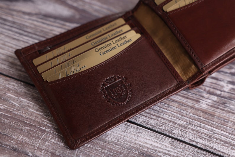 May include: A brown leather wallet with multiple card slots and a gold embossed logo. The wallet is open and the inside is lined with a beige fabric.