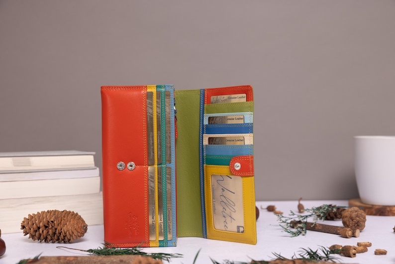 May include: A multi-colored leather wallet featuring a vibrant orange exterior, a lime green interior, and various card slots in shades of yellow, teal, and blue. The wallet includes a clear ID window, a snap button closure, and visible stitching.