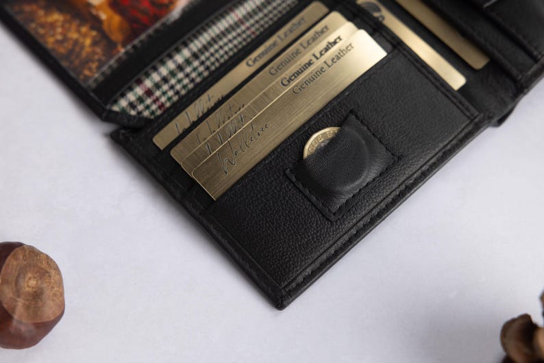 May include: A black leather wallet featuring multiple card slots, a small coin pocket with a snap closure, and a clear window section. Several gold-toned cards are inserted into the slots, each clearly marked with the text Genuine Leather.