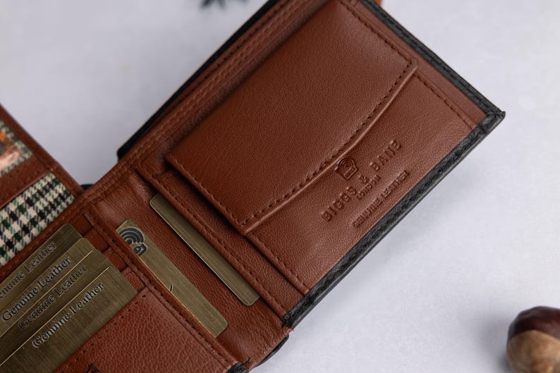 May include: A brown leather bifold wallet with a black exterior. The interior features multiple card slots, a coin pocket with a flap, and a plaid fabric lining. The wallet is embossed with the text BIGGS & BANE LONDON and GENUINE LEATHER.