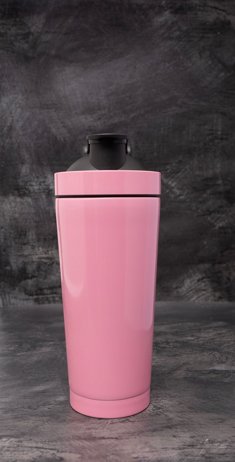 May include: A pink stainless steel shaker bottle with a black lid. The bottle is on a grey textured surface.