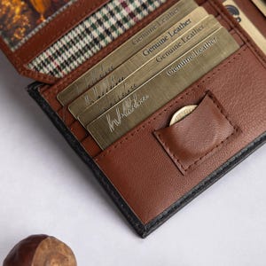 May include: A brown leather bifold wallet featuring multiple card slots, a small coin pocket, and a plaid fabric lining. Several metallic cards are inserted into the slots, each embossed with the text Genuine Leather in a repeating pattern.