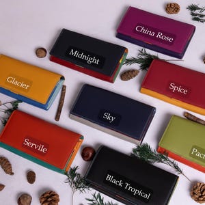 May include: A flat lay of ten colorful leather wallets with different names printed on them, including "Glacier", "Midnight", "Spice", "Sky", "Pacific", "Servile", "Black Tropical", and "China Rose".
