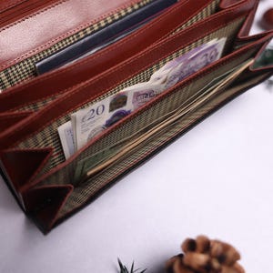 May include: A brown leather wallet with multiple compartments is open and filled with bills and cards. The wallet has a plaid lining and a zipper closure.