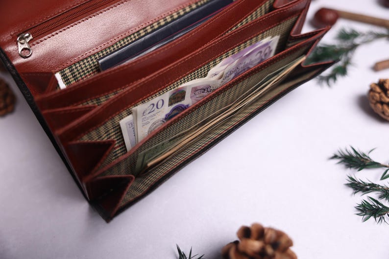 May include: A brown leather wallet with multiple compartments is open and filled with bills and cards. The wallet has a plaid lining and a zipper closure.