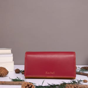 May include: A red leather wallet with a tan leather interior. The wallet has the name "Rachel" embossed on the front.
