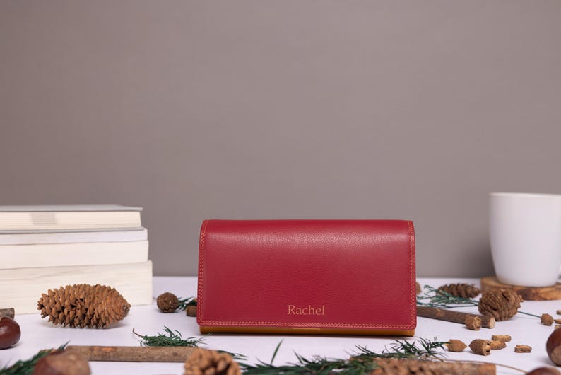 May include: A red leather wallet with a tan leather interior. The wallet has the name "Rachel" embossed on the front.