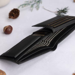 May include: A black bi-fold wallet featuring multiple interior card slots and a bill compartment lined with a black and white checkered fabric. The wallet is open to display its internal structure, including several horizontal slots for cards.