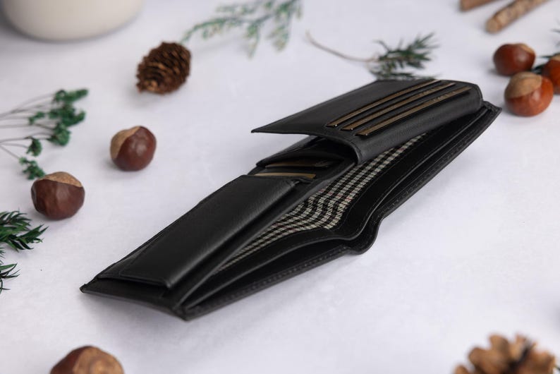 May include: A black bi-fold wallet featuring multiple interior card slots and a bill compartment lined with a black and white checkered fabric. The wallet is open to display its internal structure, including several horizontal slots for cards.