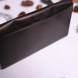 May include: A black leather clutch with a flap closure and a single pocket on the front.