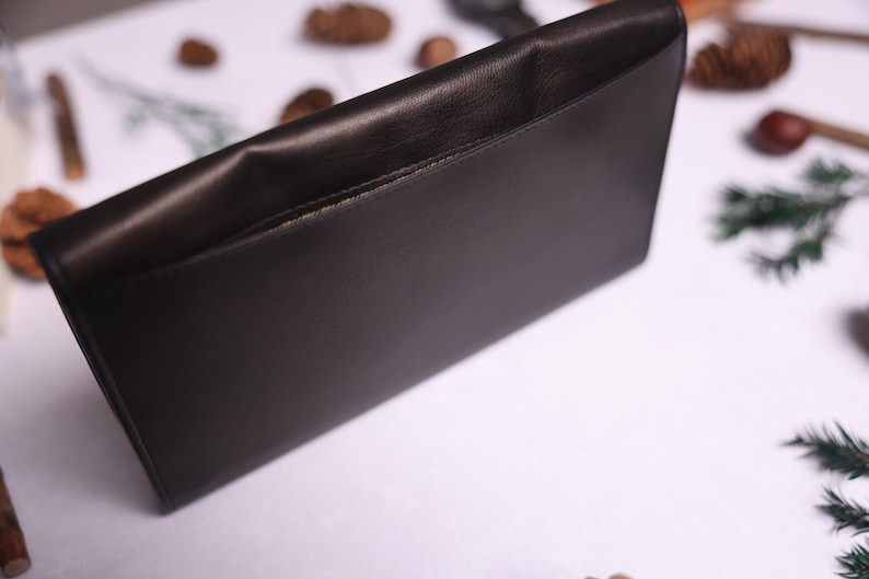 May include: A black leather clutch with a flap closure and a single pocket on the front.