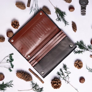 May include: A brown leather wallet with a black leather exterior. The wallet has a flap closure and multiple card slots. The inside of the wallet is lined with brown leather and has a quote engraved on it: "No matter where we travel as long as we're together every destination feels like home."