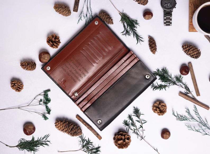 May include: A brown leather wallet with a black leather exterior. The wallet has a flap closure and multiple card slots. The inside of the wallet is lined with brown leather and has a quote engraved on it: "No matter where we travel as long as we're together every destination feels like home."