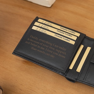 May include: Black leather wallet with a personalized message and gold-colored card slots. The wallet is open, revealing the interior with text that reads "Daddy, everything I am today is because of your love, support, and belief in me."