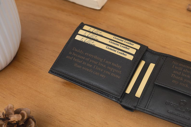 May include: Black leather wallet with a personalized message and gold-colored card slots. The wallet is open, revealing the interior with text that reads "Daddy, everything I am today is because of your love, support, and belief in me."