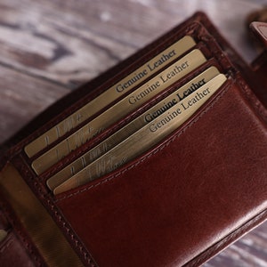 May include: A brown leather wallet with multiple card slots and a flap closure. The wallet has a gold-colored inscription that reads "Genuine Leather" on the inside.
