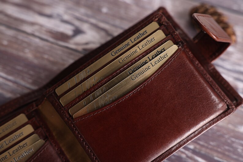 May include: A brown leather wallet with multiple card slots and a flap closure. The wallet has a gold-colored inscription that reads "Genuine Leather" on the inside.
