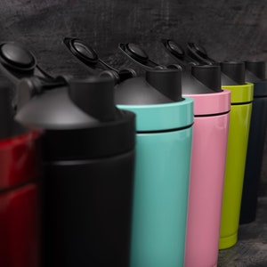 May include: A row of six colourful shaker bottles with black lids and a black band around the middle. The bottles are red, black, light blue, pink, green, and dark blue.