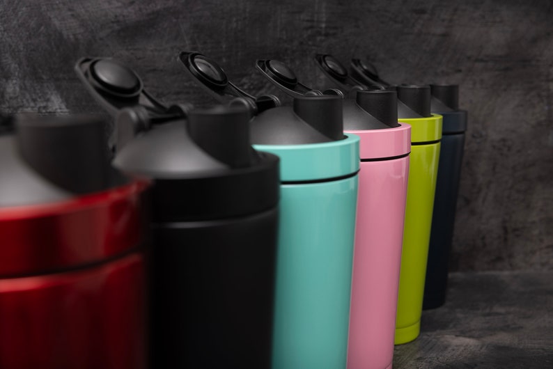 May include: A row of six colourful shaker bottles with black lids and a black band around the middle. The bottles are red, black, light blue, pink, green, and dark blue.