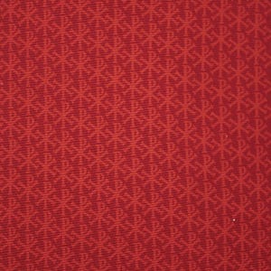 May include: Close-up of a red fabric with a repeating pattern of stylized symbols. The symbols are a lighter shade of red, creating a subtle contrast. The fabric has a textured appearance.