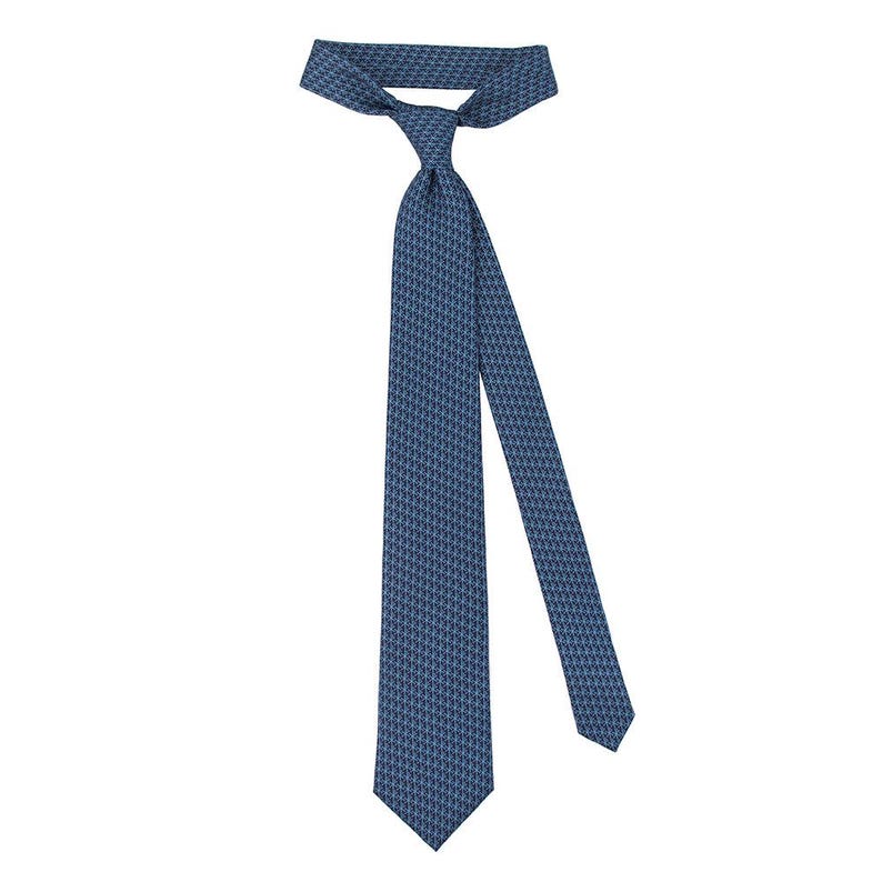 May include: A navy blue tie with a repeating geometric pattern. The tie is knotted and hangs diagonally against a white background. The tie's design is a small, intricate pattern in a slightly lighter shade of blue.