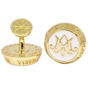 May include: Gold-toned cufflinks with religious symbols. One cufflink features a cross-like design on a round top, the other has a white center with a stylized 'M' and surrounding text. The cufflinks are likely made of metal.