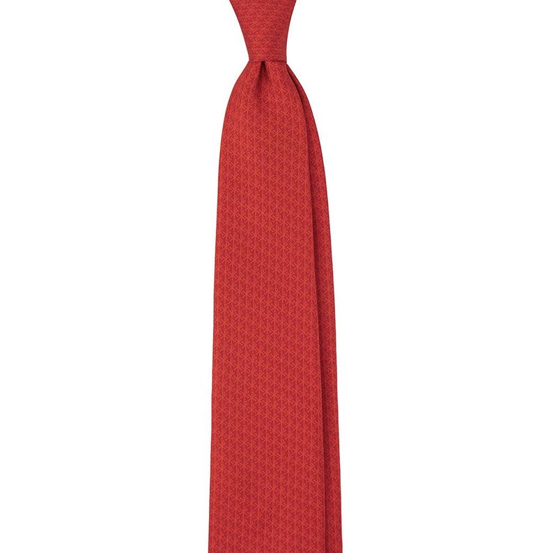May include: A solid red necktie with a subtle geometric pattern. The tie is knotted at the top and hangs vertically against a white background. The fabric appears to be a woven material.