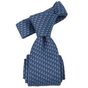 May include: A navy blue tie with a repeating light blue pattern. The pattern consists of a stylized cross and the Greek letters Chi and Rho. The tie is knotted and folded, showcasing the intricate design.