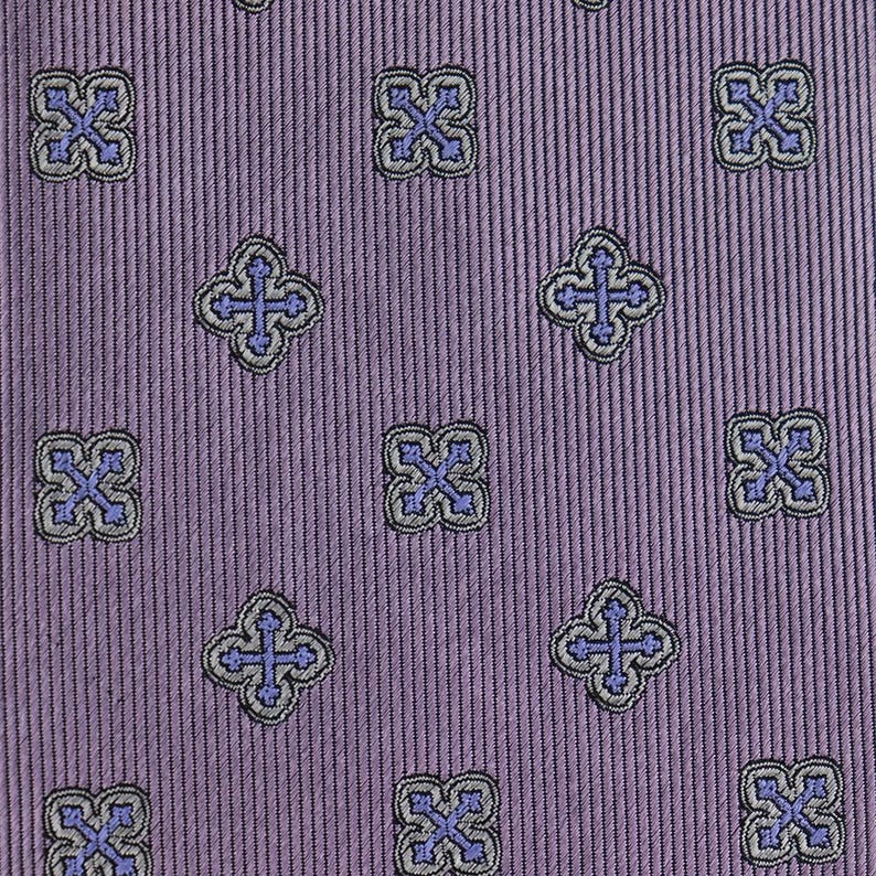 May include: Purple fabric with a repeating pattern of small, blue and gray crosses in a square shape.