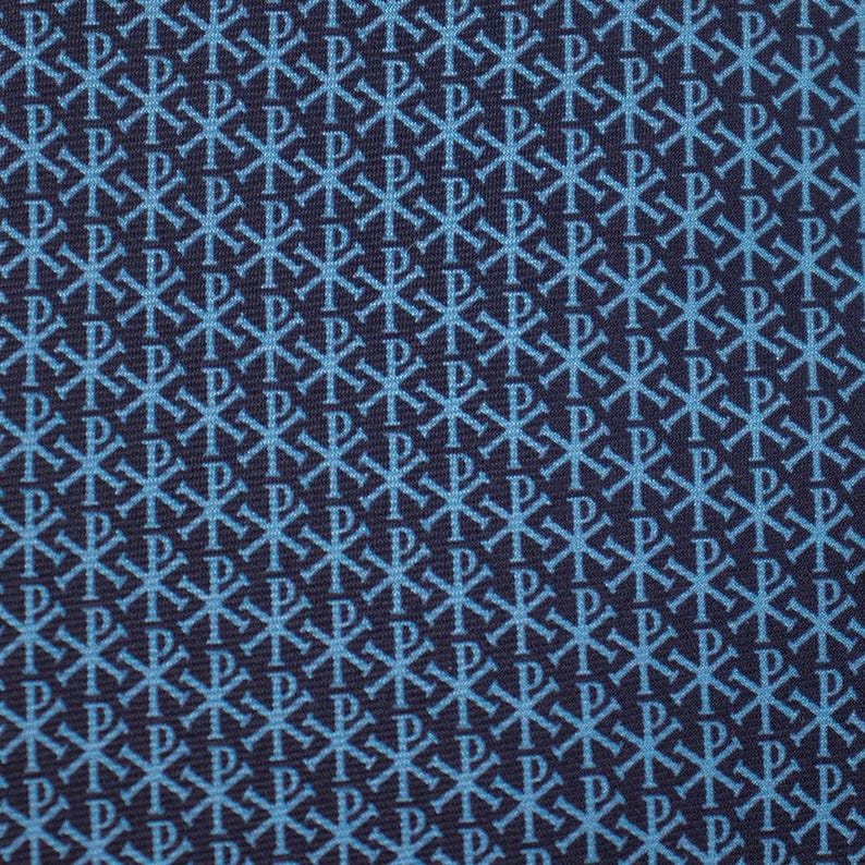 May include: Close-up of a navy blue fabric with a repeating pattern of light blue symbols. The symbols are a combination of a cross and the letter "P", creating a textured design. The fabric has a subtle sheen.