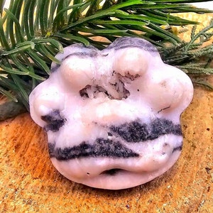 May include: A pink and black banded agate with a natural crystal formation inside. The agate is smooth and polished.