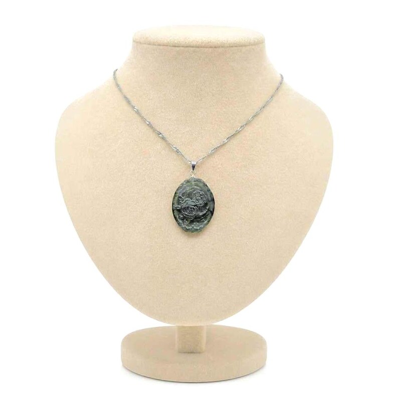 K&ouml;nnte beinhalten: Eine silberfarbene Kette mit einem ovalen Anh&auml;nger. Der Anh&auml;nger besteht aus einem dunkelgr&uuml;nen Stein mit einem eingravierten Blumenmuster auf der Oberfl&auml;che. Die Kette ist d&uuml;nn und metallisch und mit einer silbernen &Ouml;se am Anh&auml;nger befestigt.