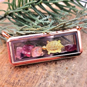 May include: A rose gold locket with a clear glass window, containing pink and purple crystals and a gold turtle charm.