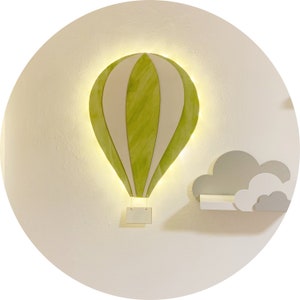 Könnte beinhalten: Eine grüne und weiße Heißluftballon-Wanddekoration mit einem Licht im Inneren. Der Ballon hat ein weißes Schild, das daran hängt. Der Ballon ist an einer weißen Wand mit einem weißen Wolkenregal befestigt.