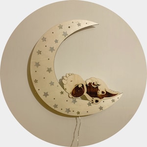 Può includere: Una luna di legno a forma di mezzaluna con un dinosauro che dorme e stelle ritagliate. La luna ha una ghirlanda di luci.