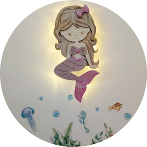 May include: A wooden mermaid wall decor with a light-up feature. The mermaid has long, light brown hair, a pink bow, and a pink tail. The background features underwater-themed stickers, including a jellyfish, seahorse, and fish.