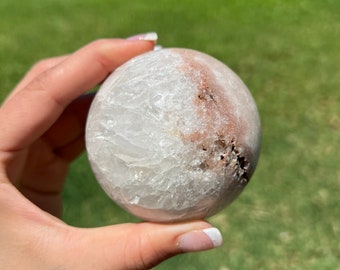 Puede incluir: Una esfera de selenita blanca y rosa con una superficie rugosa y texturizada. La esfera es aproximadamente del tamaño de una pelota de béisbol.