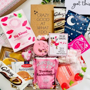 May include: A gift box containing a variety of items including a brown box labeled Uni Survival Kit, a bag of Big Kisses gummies, a packet of Galaxy hot chocolate, a Steam Eye Mask, a card saying you've got this, and a bag of Popcorn Shed marshmallows.