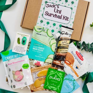 May include: A cardboard gift box labeled Jack's Uni Survival Kit containing a variety of items including a cucumber mud mask, Galaxy instant hot chocolate, Daelmans stroopwafel, Candy Kittens sour watermelon candy, Pukka tea bags, and a pickle pin.