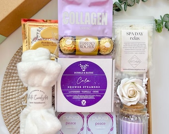 May include: A gift box filled with spa day items. Includes a white spa headband, bath salts, shower steamers, a candle, eye masks, chocolates, and collagen supplements. The box is decorated with a sprig of eucalyptus.