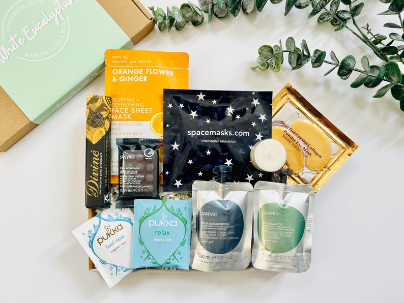 May include: A gift box filled with self-care items, including face masks, tea bags, bath products, and chocolate. The box is decorated with a green and white label that says "White Eucalyptus".