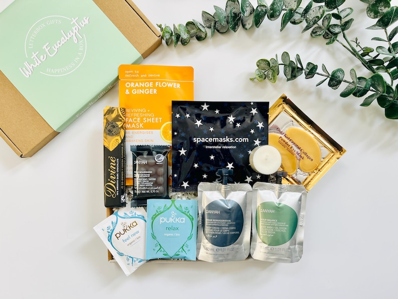 May include: A gift box filled with self-care items, including face masks, bath products, tea, and chocolate. The box is decorated with a green label that says "White Eucalyptus".
