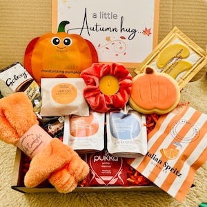 May include: A gift box labelled A little Autumn hug containing a pumpkin face mask, a red velvet scrunchie with a yellow tea light, a pumpkin-shaped cookie, gold eye masks, a Galaxy hot chocolate sachet, orange headband, tea bags, and Italian Spritz gummies.